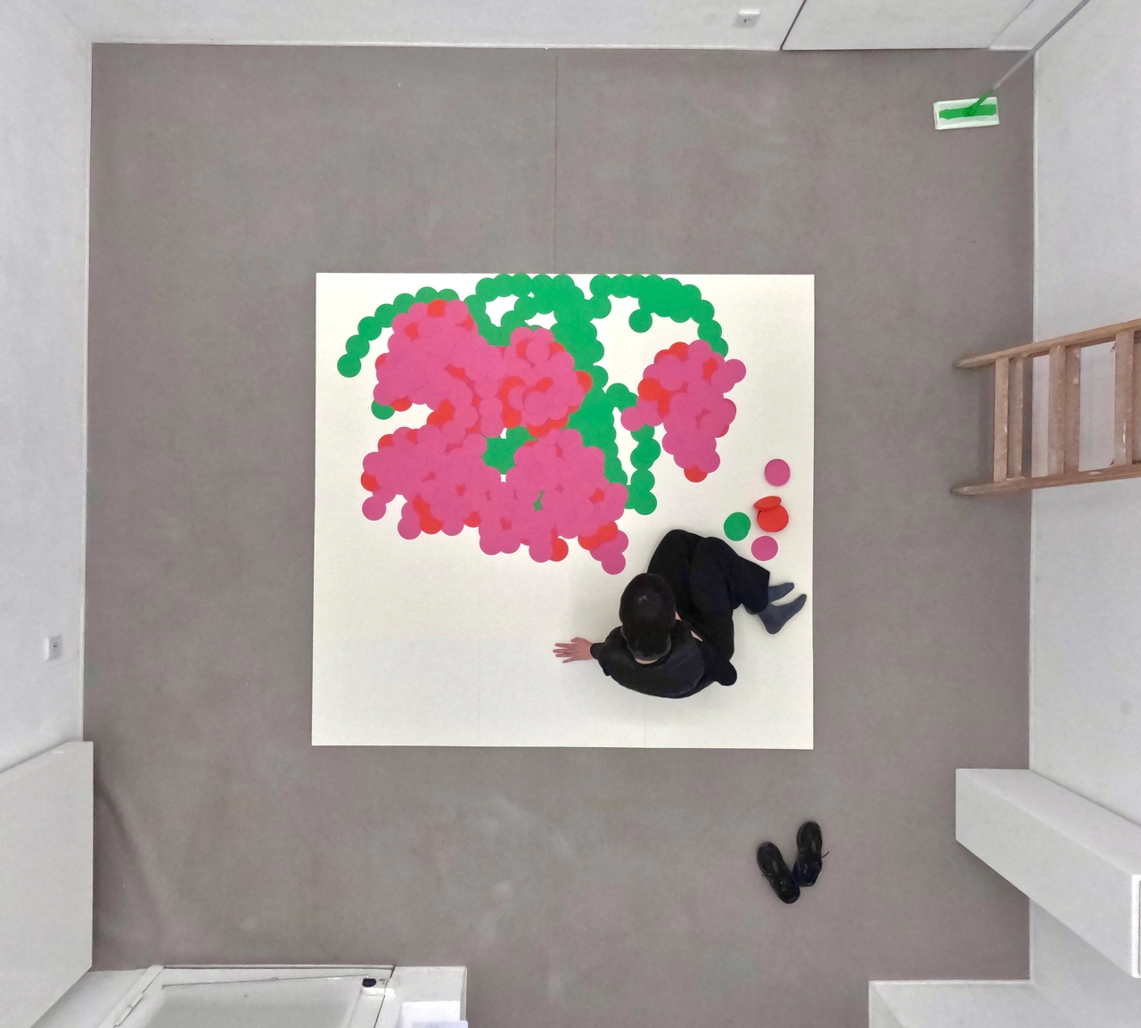 Artist Ayong Son sits on the floor beneath a large paper artwork featuring pink and green abstract organic shapes