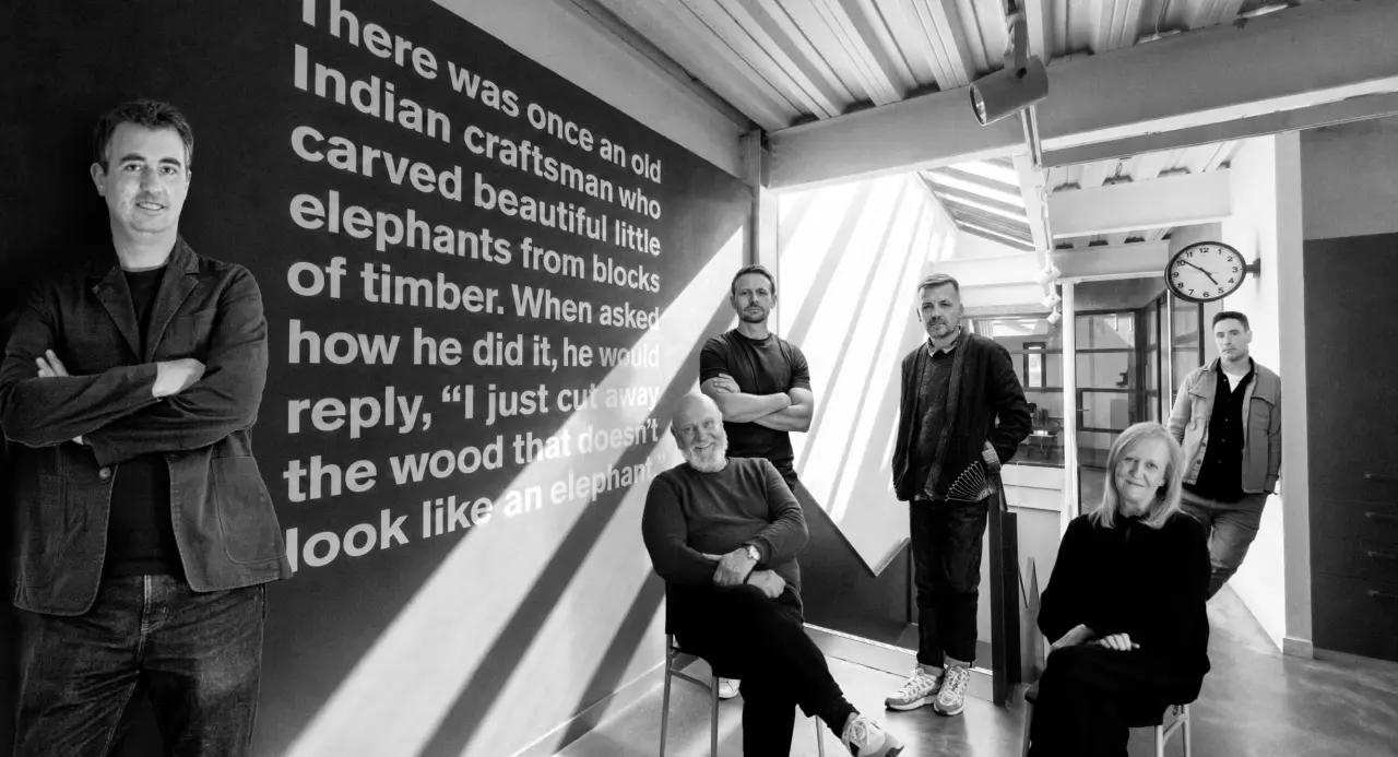 Team of creatives standing in an office space next to a wall featuring a quote about Indian craftmanship and carved wooden elephants