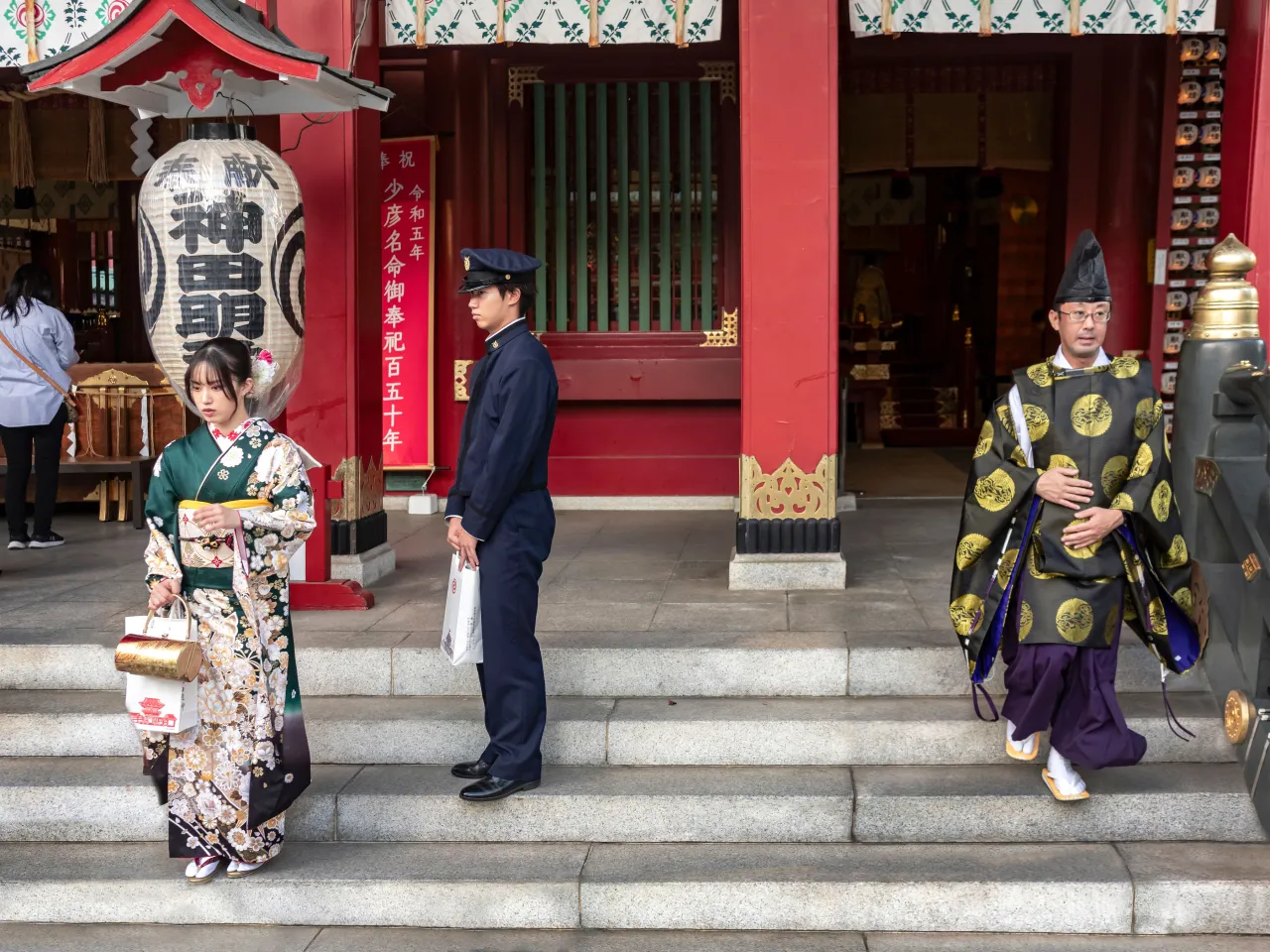 Kanda Myojin Shrine with a history of more than 1,300 years as the chief Shinto shrine of Edo since the Edo period. A young girl poses for dad taking a photograph, while a priest leaves the temple. Chiyoda City, Tokyo