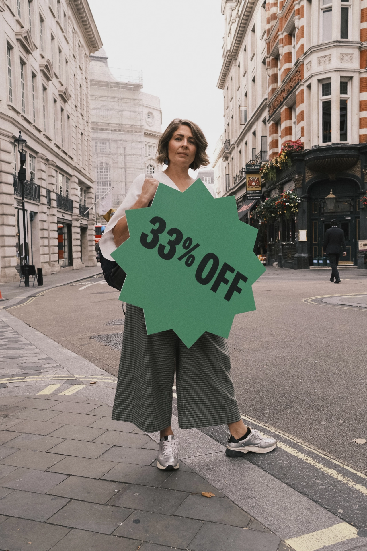 Woman holding a large green starburst sign reading "33% OFF" on a London street, highlighting the pension gap between men and women