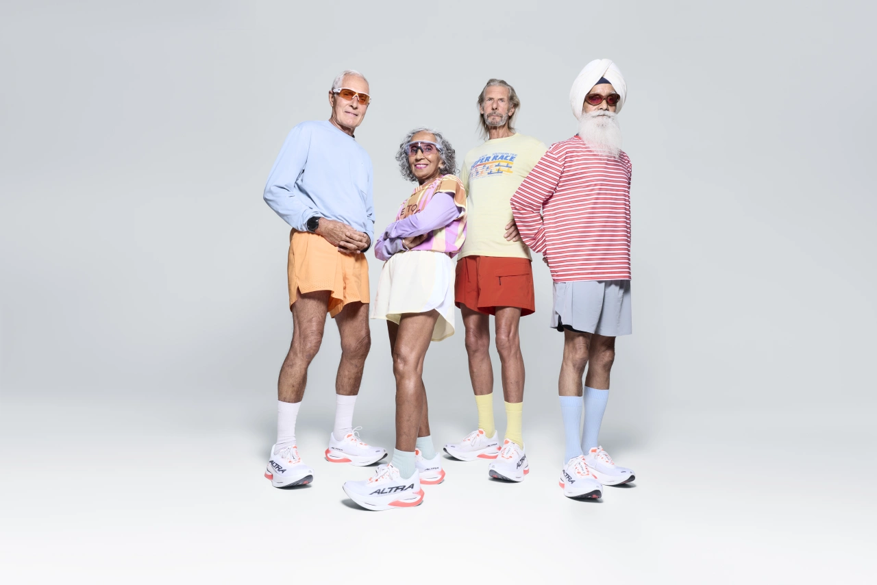 Four older runners aged 75 to 85 stand together wearing colourful trainers, shorts and tops against a white background