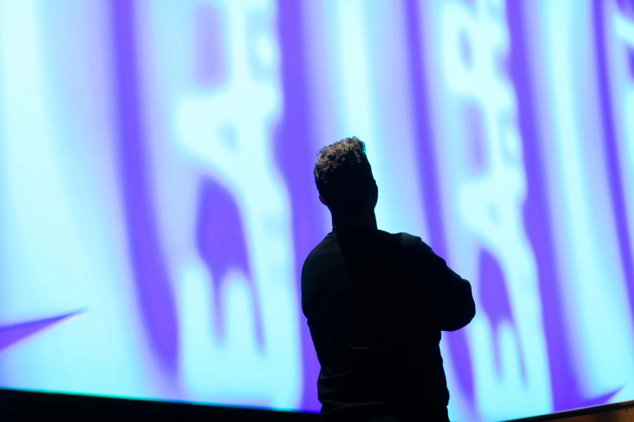 Silhouetted figure stands facing a large screen displaying abstract purple and blue light projections