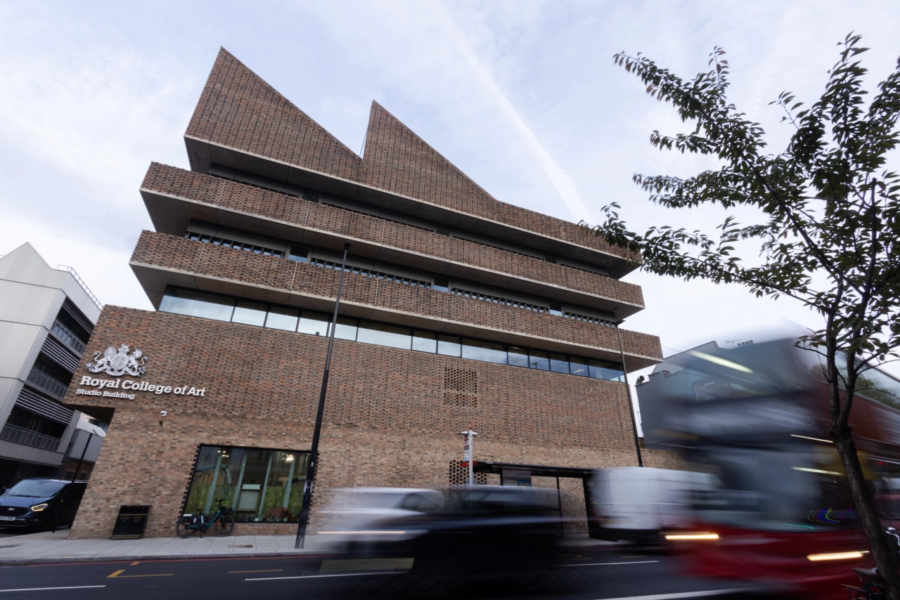 Royal College of Art's Battersea campus building with distinctive stacked brick tiers and large windows, with buses passing on the street below