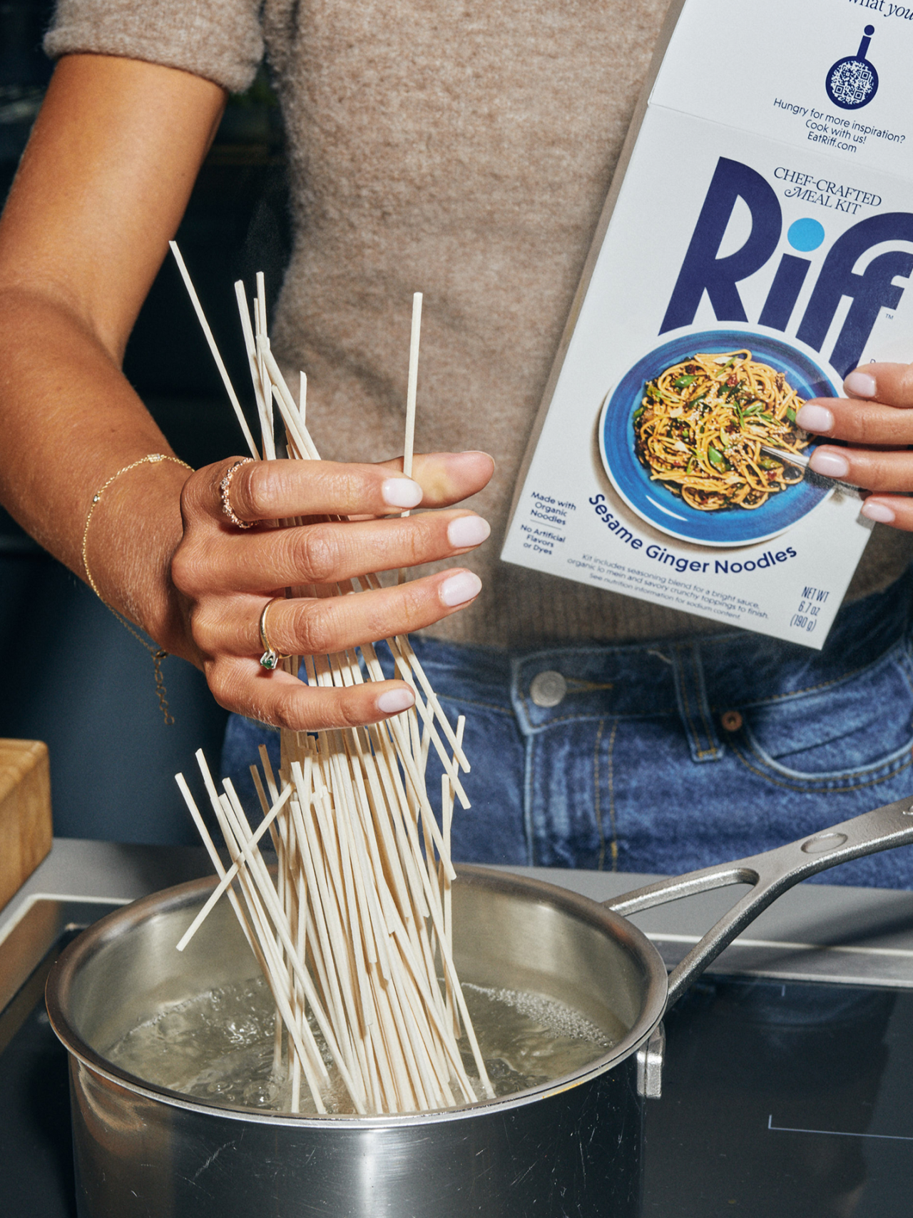 Person holding a package of Riff Sesame Ginger Noodles above a pot of boiling water with noodles being added to it