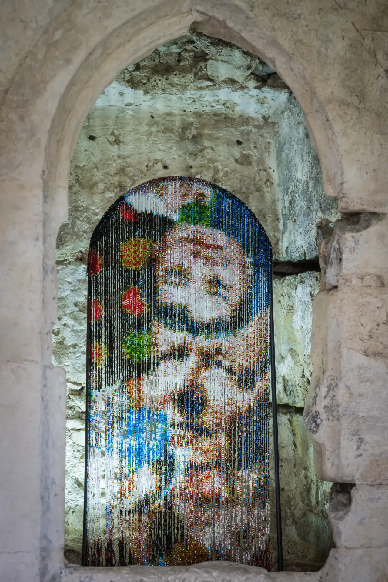 Lily Bunney's pixelated painting of a face with colourful geometric patterns displayed in an arched stone alcove within Norwich Cathedral's ancient walls
