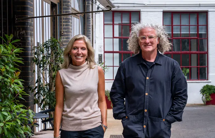 Kate Cox, CEO, and Wayne Deakin, Chief Creative Officer, standing in a modern courtyard with brick and white buildings behind them