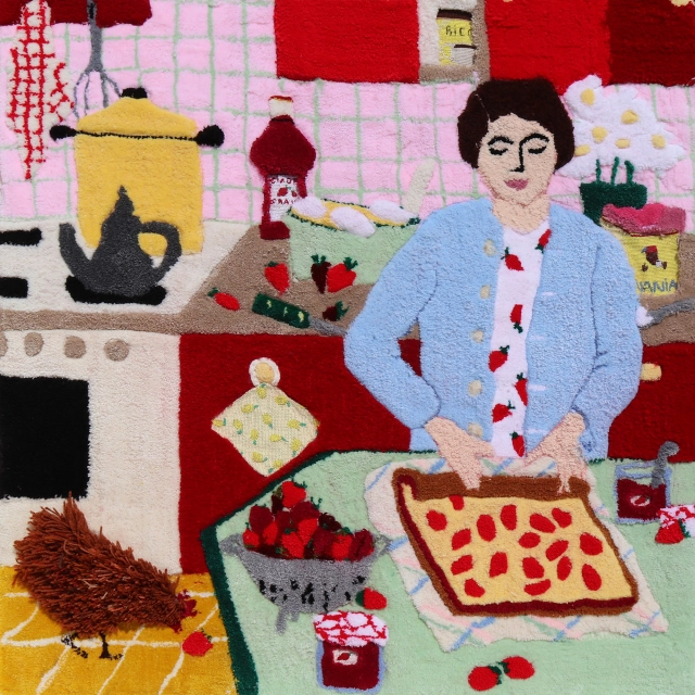 Textile artwork depicting a woman in a blue cardigan preparing a red-spotted roll cake in a colourful kitchen filled with cooking utensils and ingredients