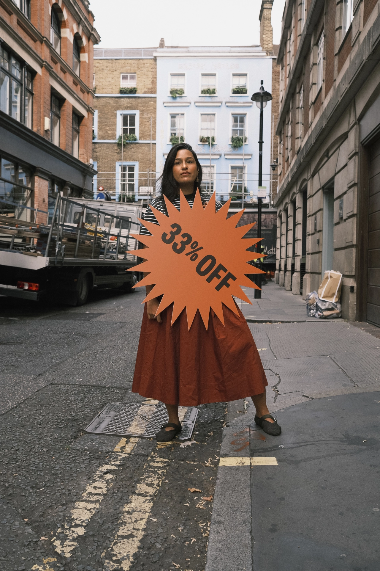 Woman holding an orange starburst sign reading "33% OFF" in a London street, highlighting the gender pension gap campaign by Pregnant Then Screwed