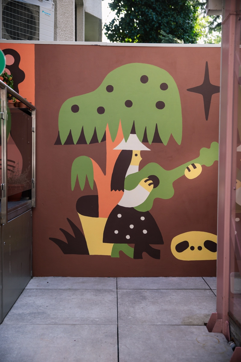 Colourful mural featuring a stylised figure with green hair playing a yellow-green guitar, surrounded by abstract shapes and a creature with yellow eyes on a burgundy background