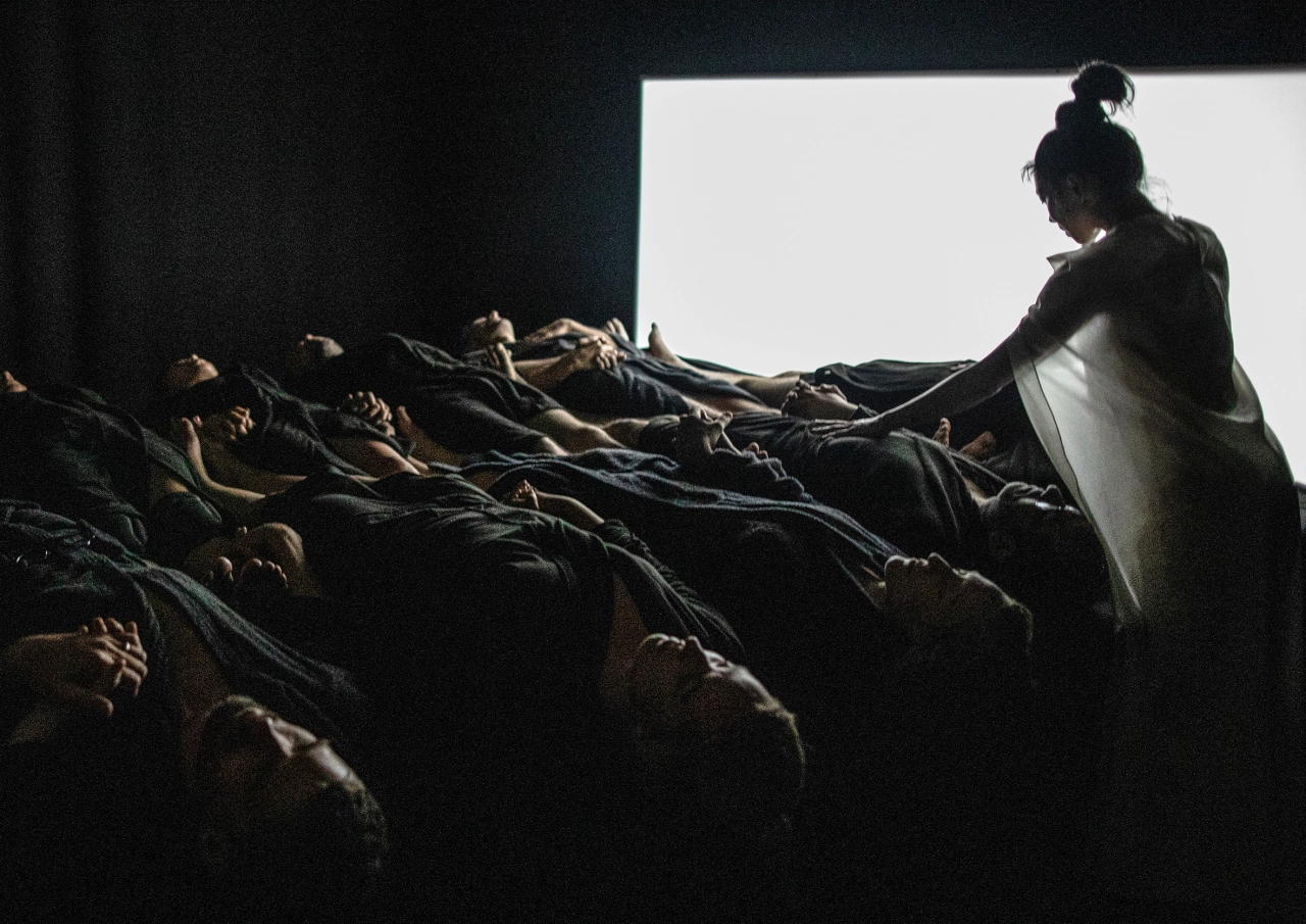 A dancer in dark clothing arranges participants lying on the ground during the immersive Chapter Five/KAIHOGYO experience