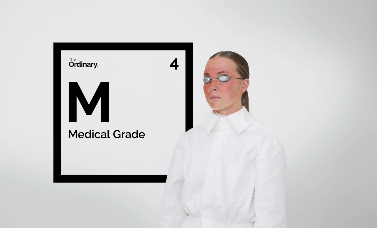 Person in white shirt and glasses standing next to a parody periodic table element reading "M Medical Grade" with "Ordinary" branding and number 4