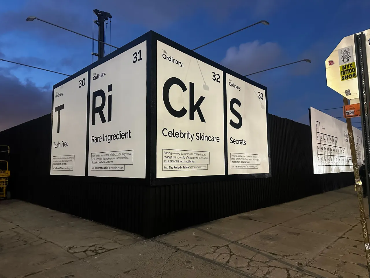 Outdoor advertising billboard with periodic table design spelling "Tricks" and "Secrets", parodying beauty industry marketing buzzwords