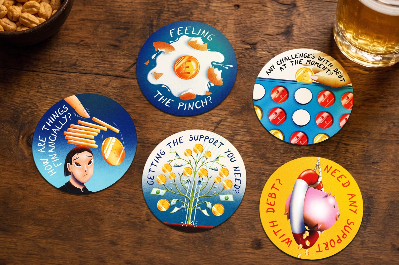 Five illustrated coasters with debt-related messages displayed on a wooden table alongside snacks and beer, part of Lowell's Say It Over a Drink campaign