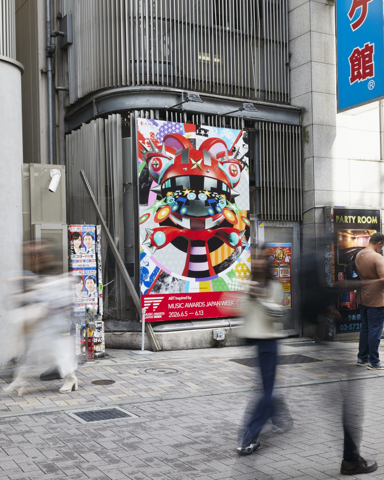 Vibrant red and colourful poster for Music Loves Art 2026 displayed on a building exterior in a busy Tokyo street with pedestrians passing by