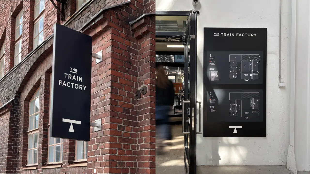 The Train Factory storefront with navy signage and wayfinding panel mounted on red brick building exterior