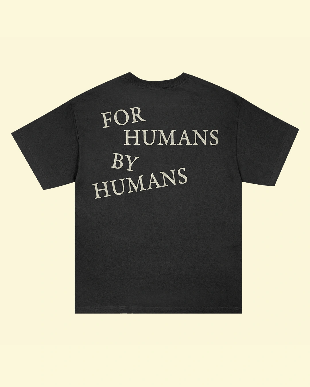 Black t-shirt printed with white text reading "FOR HUMANS BY HUMANS" on the back, displayed against a cream background