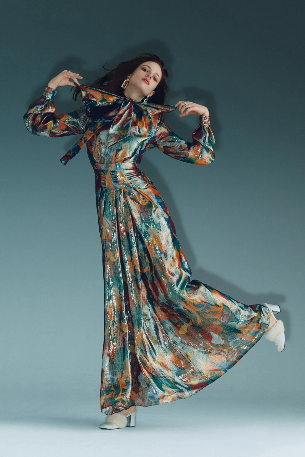 Woman wearing a vibrant multicoloured patterned dress with flowing skirt and puffed sleeves, posing against a teal background