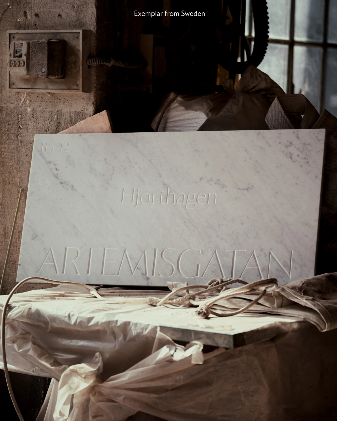 Marble stone tablet inscribed with "Iljorhagen" and "ARTEMISGATAN" text, leaning against a brown fabric bag in an indoor setting