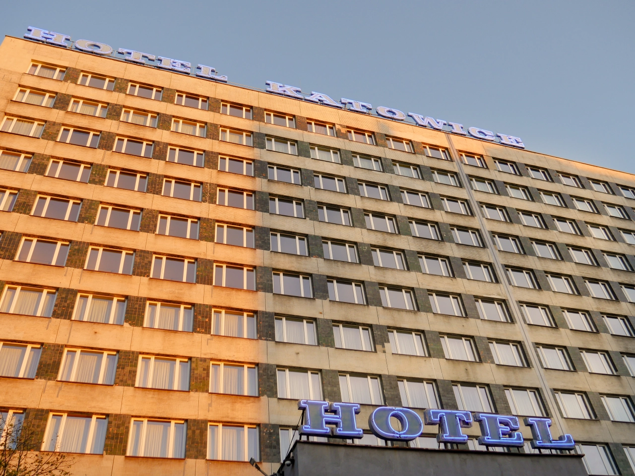 Hotel Katowice in Poland, a multi-storey brutalist building with a split orange and grey facade and "HOTEL" sign at ground level against a clear blue sky