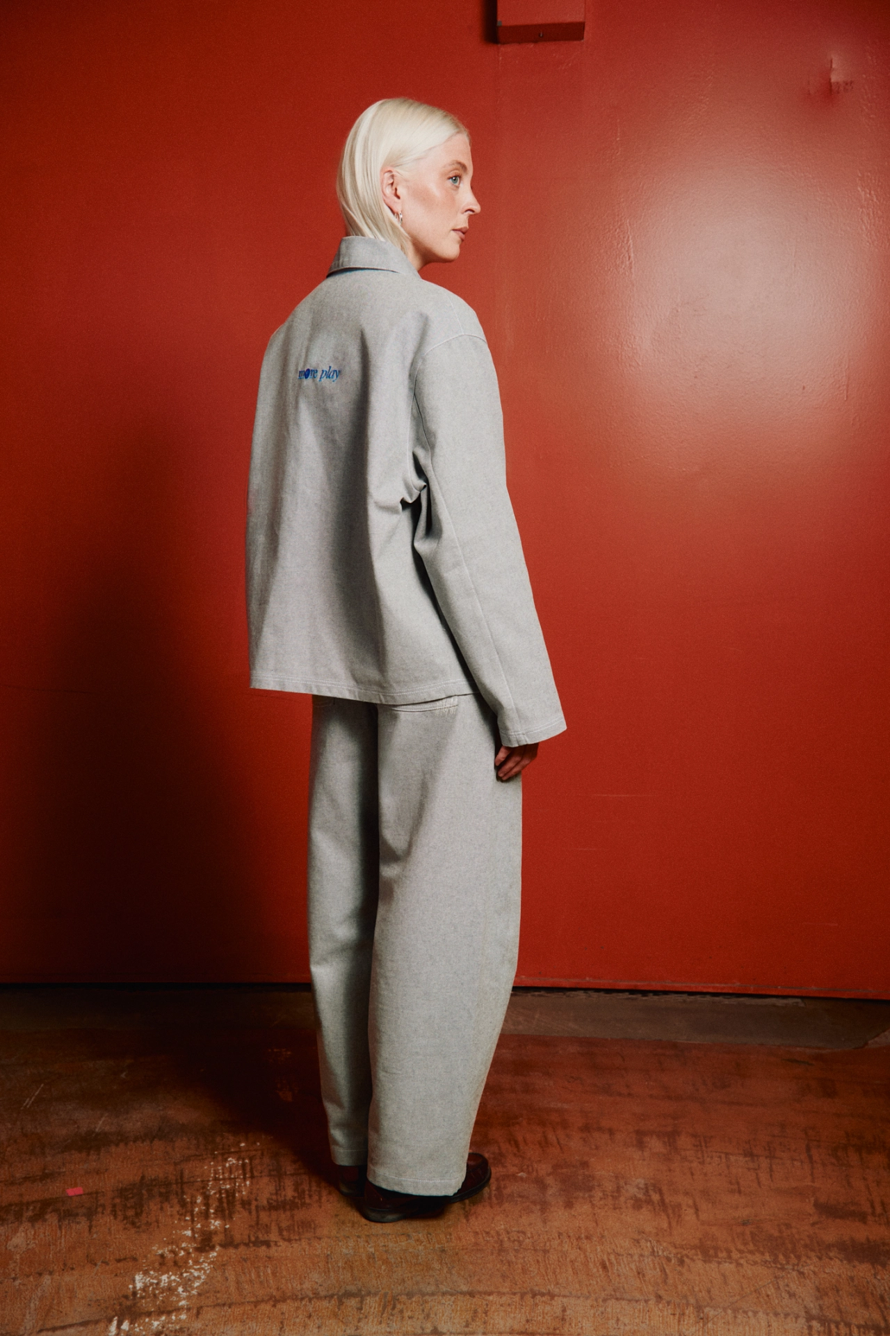 Person viewed from behind wearing a light grey oversized blazer and matching wide-leg trousers against a red wall