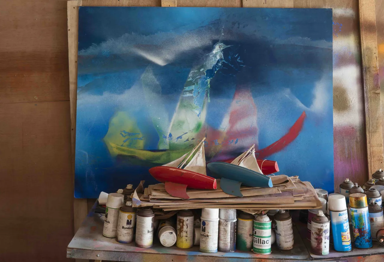 Sidney Nolan painting of colourful boats displayed above a wooden shelf containing numerous paint cans and art materials from his studio at The Rodd