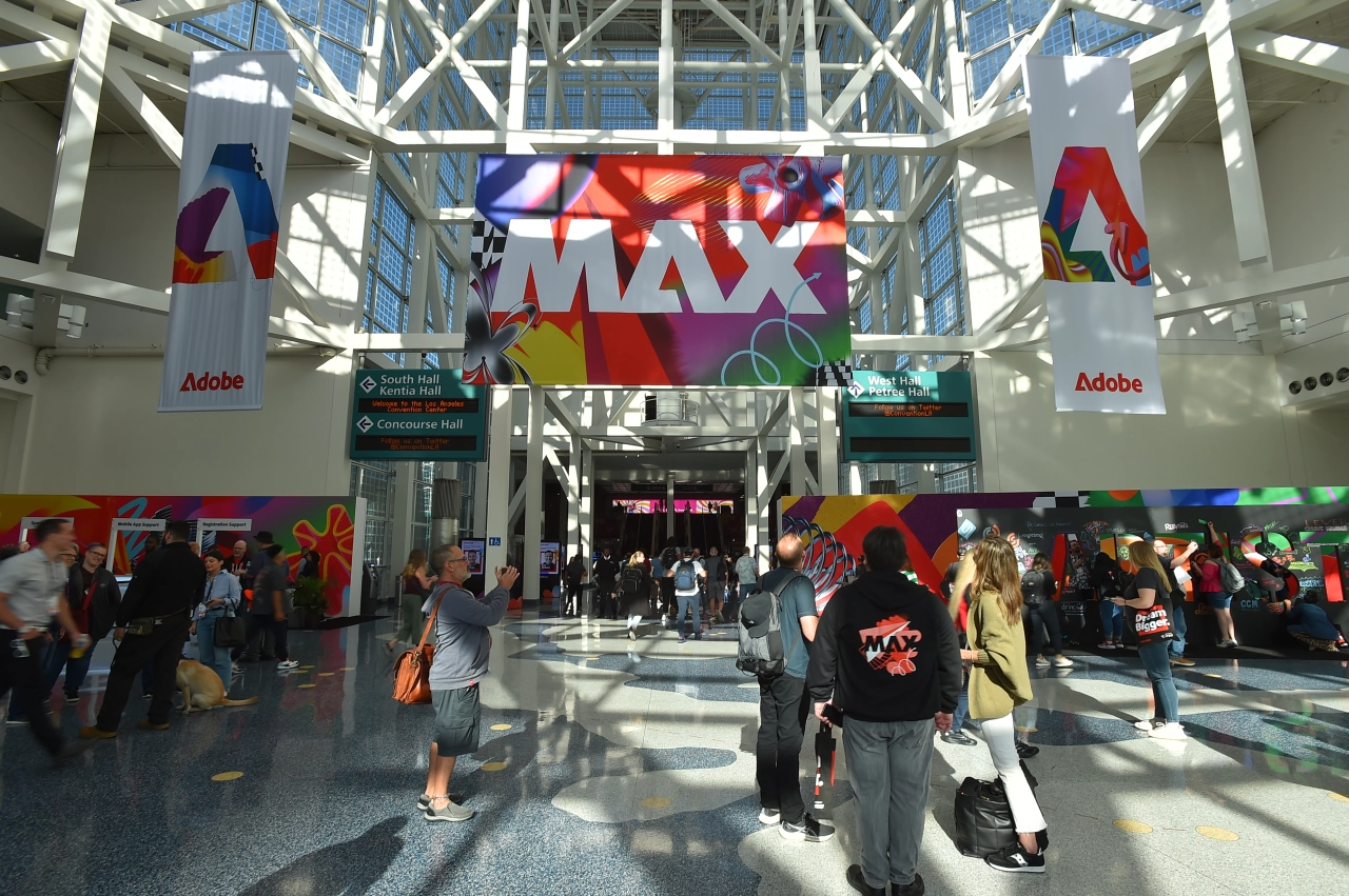Adobe MAX conference venue in Miami with colourful branding banners and Adobe logos suspended from the ceiling, attendees walking through the modern architectural space
