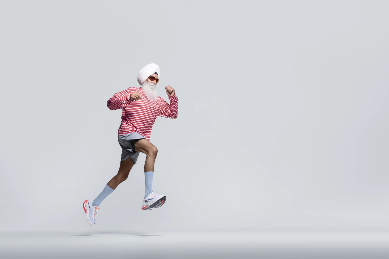 Runner in pink striped top, white cap and socks mid-stride against a grey background