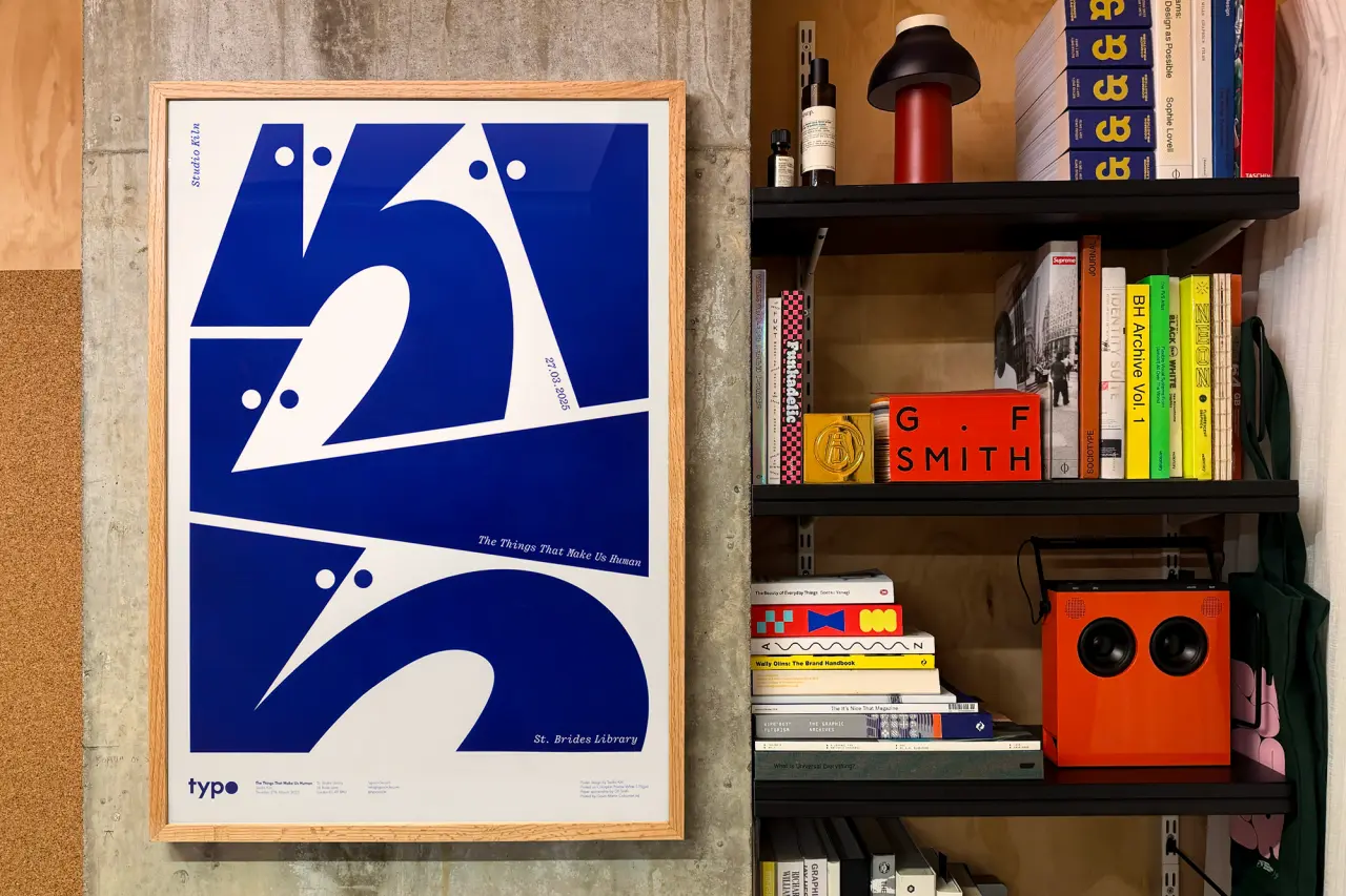 Blue and cream geometric poster with the number 25 displayed on a shelf next to design books and an orange speaker