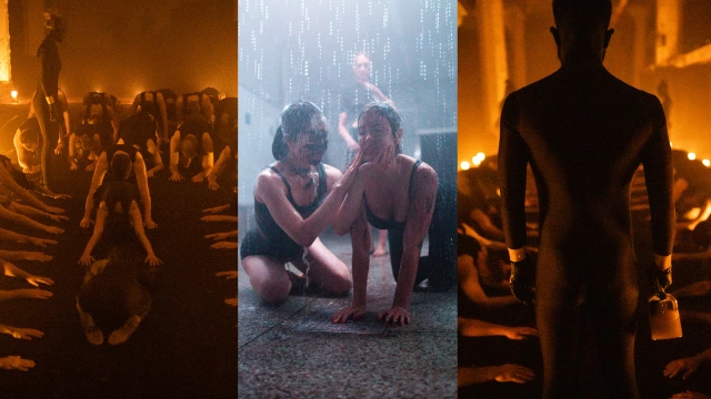 Nude figures in a dimly lit warehouse space with orange lighting, some sitting and others standing in silhouette during an immersive art experience.