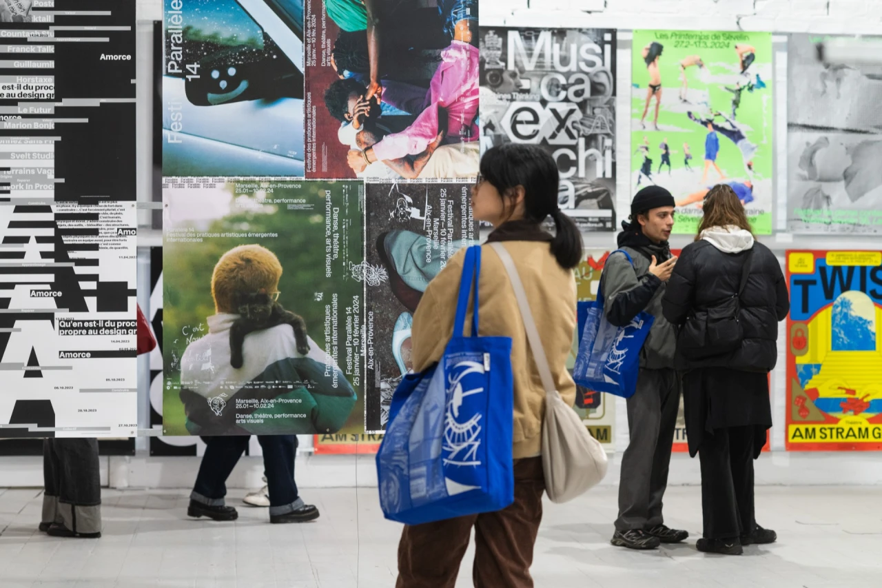 Visitors view posters and artwork displayed on a white gallery wall at International Assembly festival in Glasgow