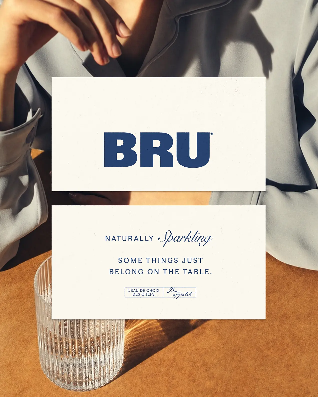 Person holding a BRU sparkling water brand card displaying the logo and tagline "Naturally sparkling, some things just belong on the table