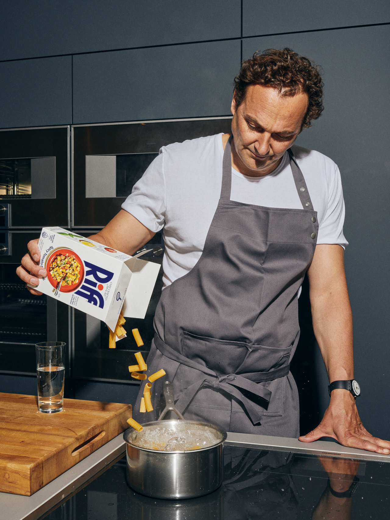 Man in grey apron pouring Riff pasta into a pot of water in a modern kitchen