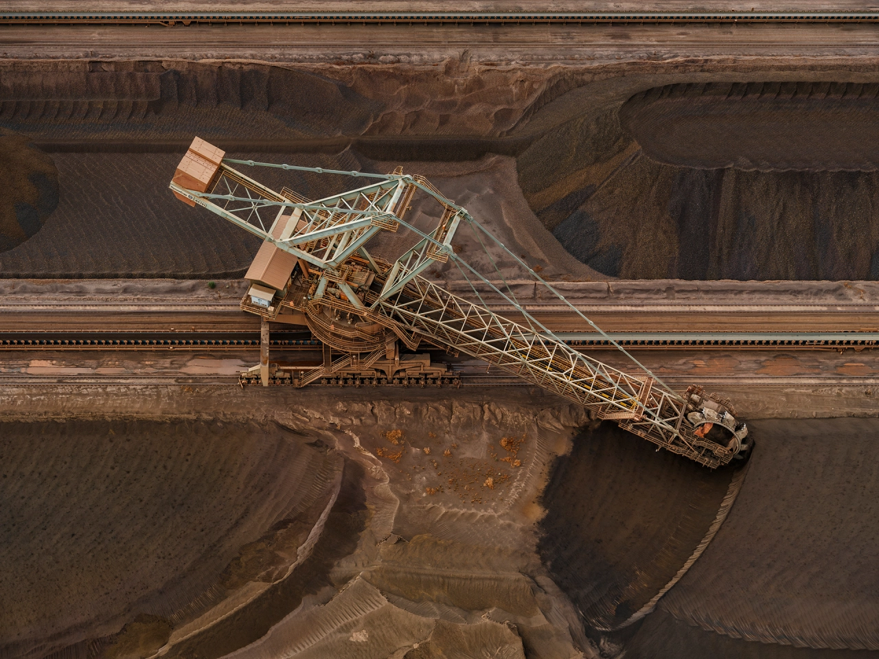 Aerial view of a massive excavator positioned on the edge of an open-pit mine with exposed mineral deposits and earthen walls below