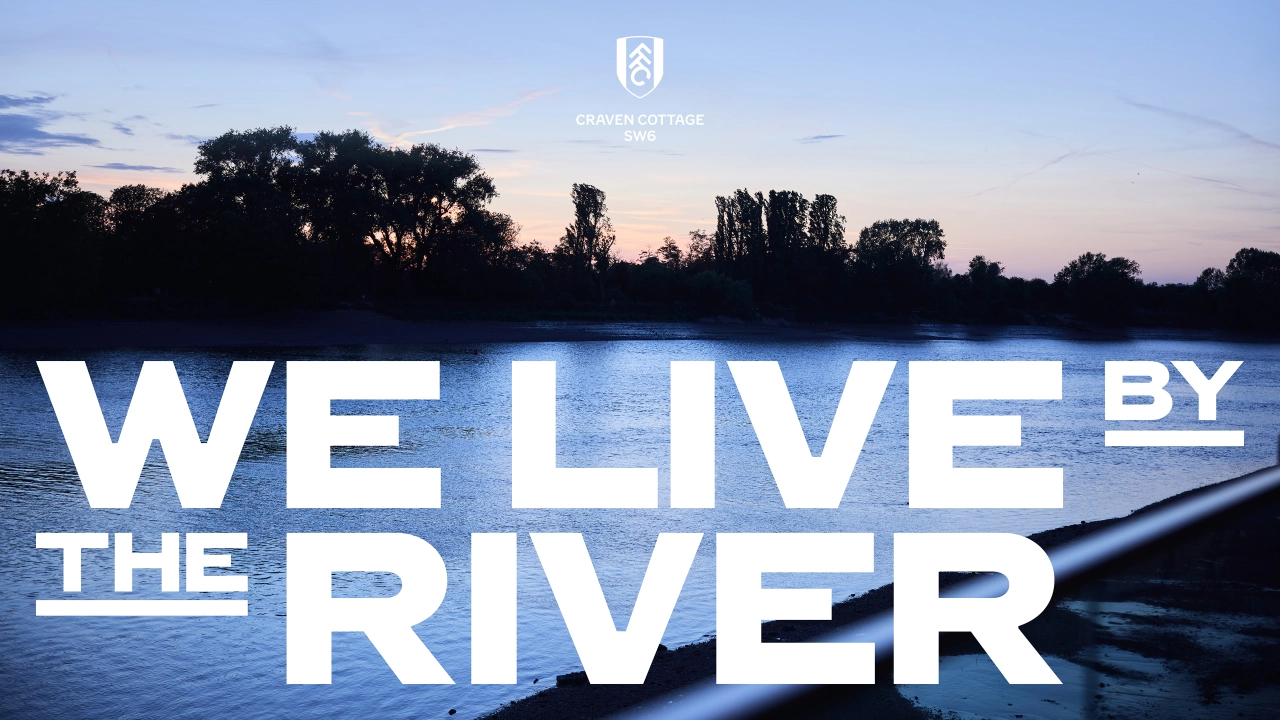 Twilight view of a river with silhouetted trees and a moored boat, overlaid with white text reading "We live by the river