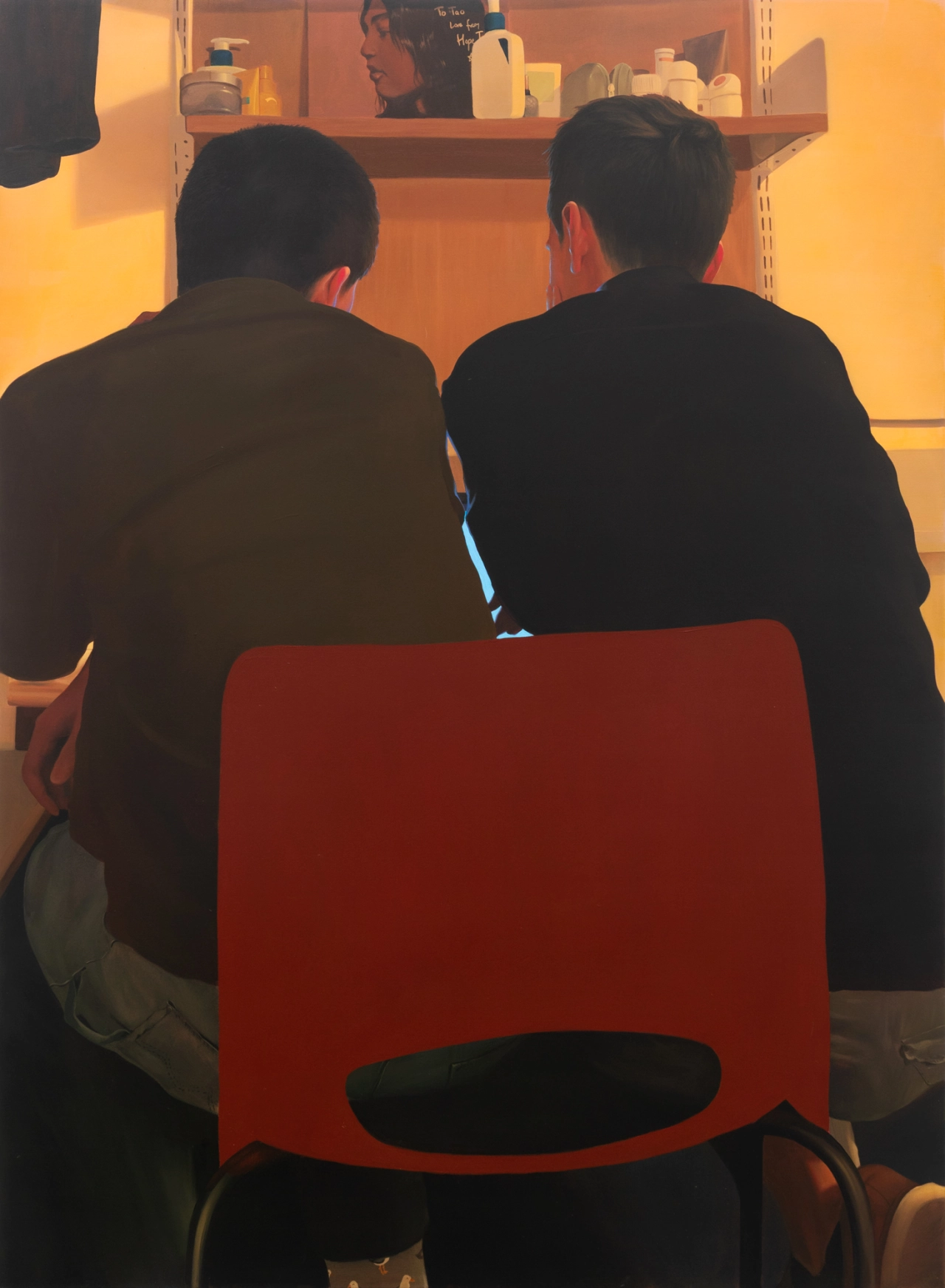 Two figures sit back-to-back on a red chair, viewed from behind against a warm orange-lit interior with shelving