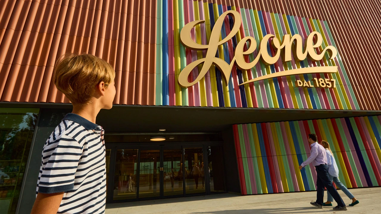 Young child in striped t-shirt viewing the colourful Leone storefront with vertical rainbow stripes and illuminated gold script signage