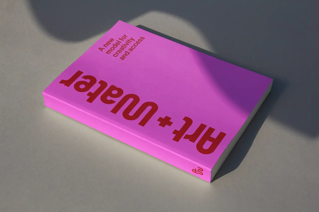 Bright pink book cover for Art + Water with reversed text and small descriptive text at top, casting shadows on grey surface