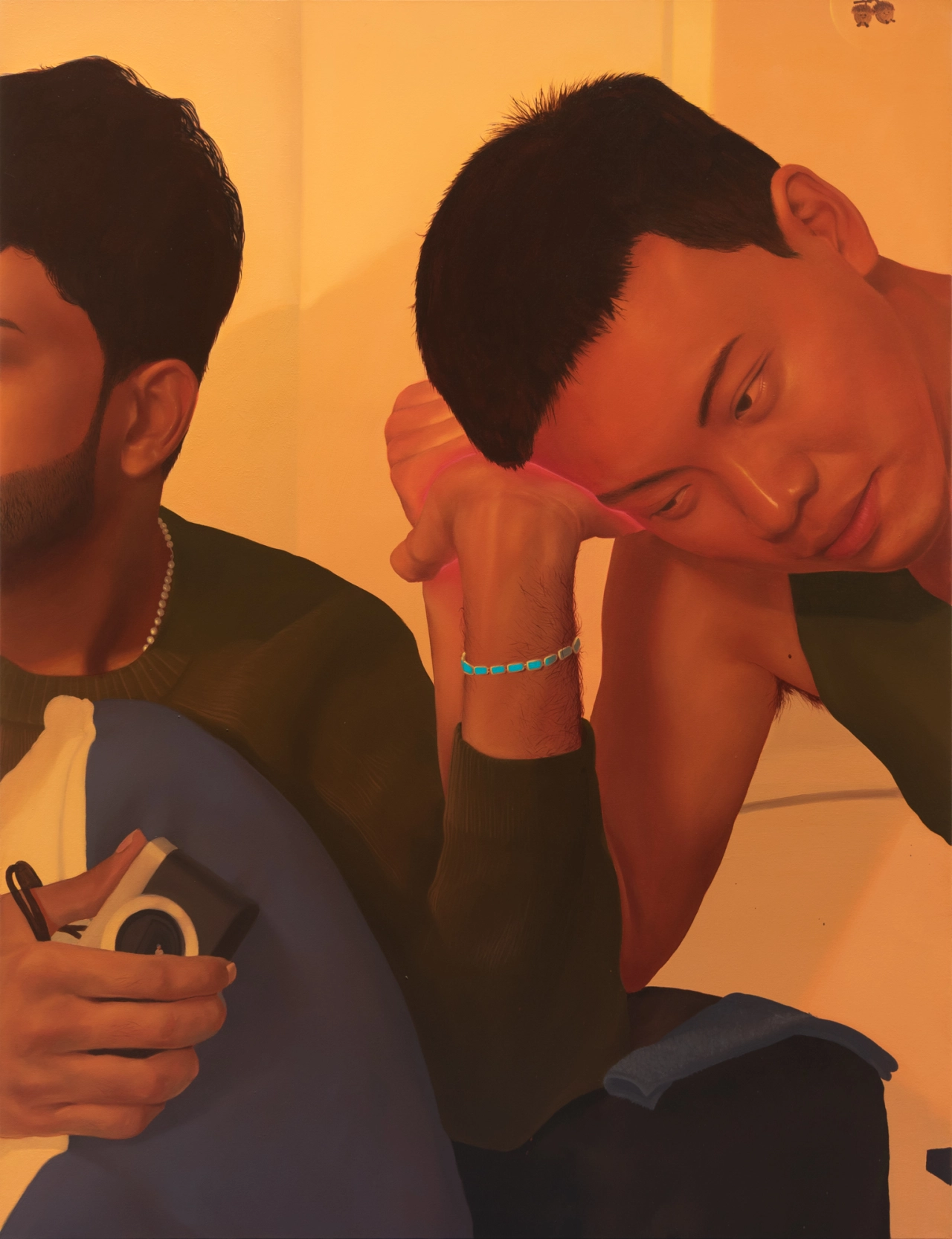 Two men with warm-toned skin posed against a golden-orange background, one wearing a turquoise beaded bracelet and looking downward pensively