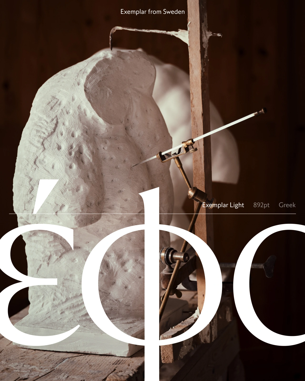 A marble torso sculpture lit by a single light source, mounted on a wooden frame with measurement tools, showing the Exemplar typeface carved into the surface