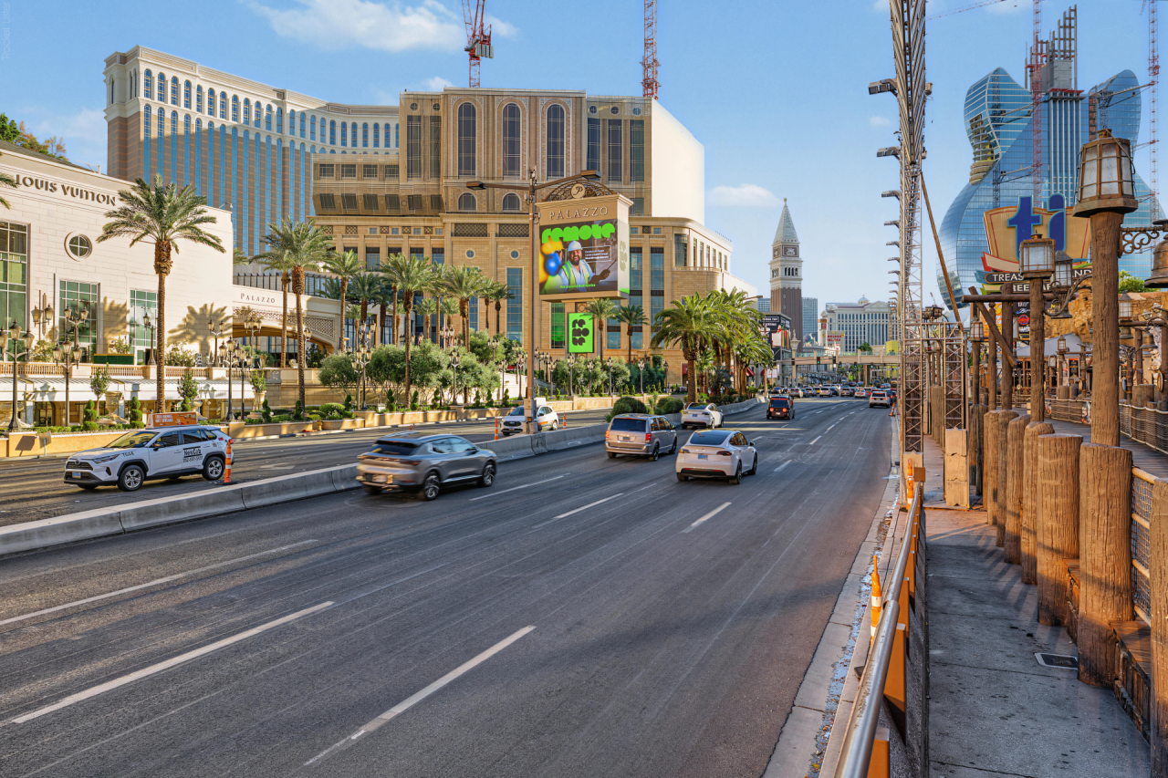 The Las Vegas Strip with casinos, palm trees and vehicles on a wide boulevard under a blue sky