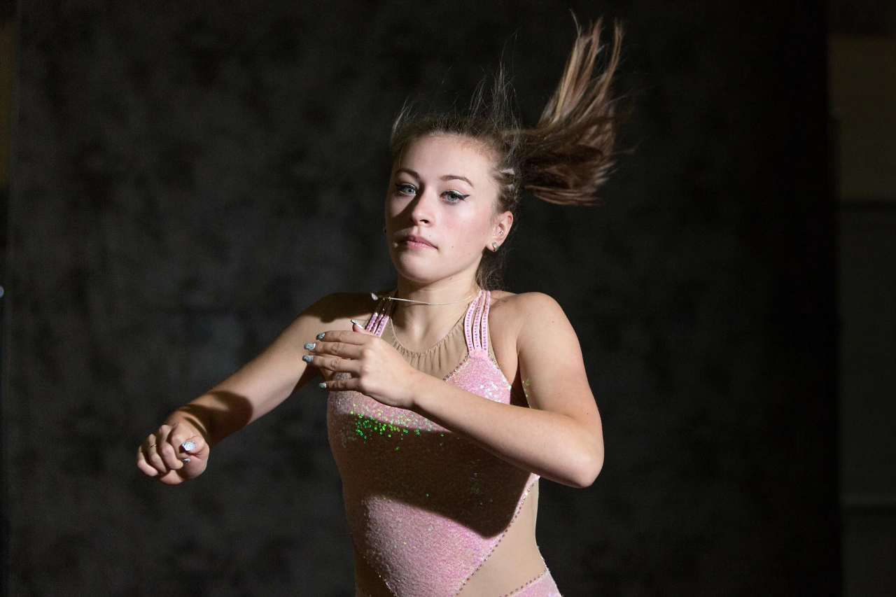 Young roller skater in pink athletic wear with hair flying upward, captured mid-motion against a dark background