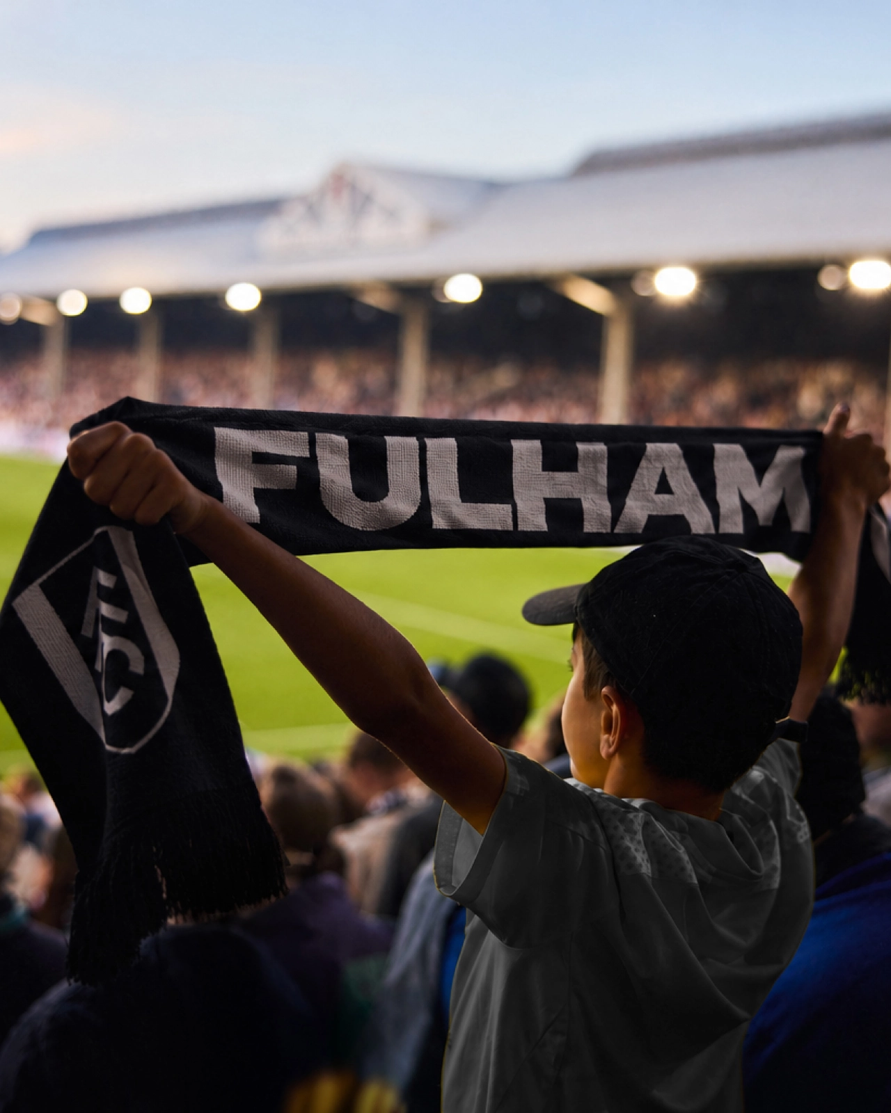 Fulham FC supporter holding up a black scarf with white "FULHAM" lettering at Craven Cottage stadium