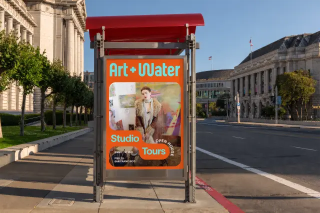 Art + Water Studio Tours advertisement on a San Francisco bus shelter, featuring an orange background with cyan lettering and an image of a person in a studio space