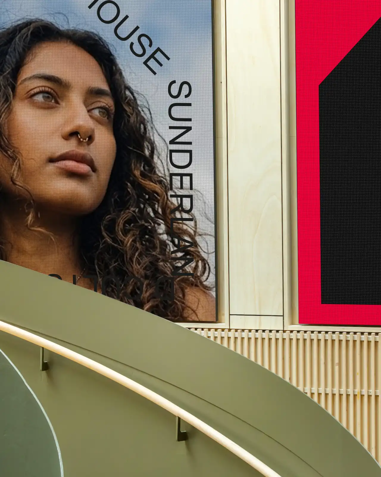 Woman with wavy dark hair and nose ring gazing upward on a large interior sign with "OUSE SUNDER" text visible, alongside minimalist geometric shapes in cream, olive and hot pink