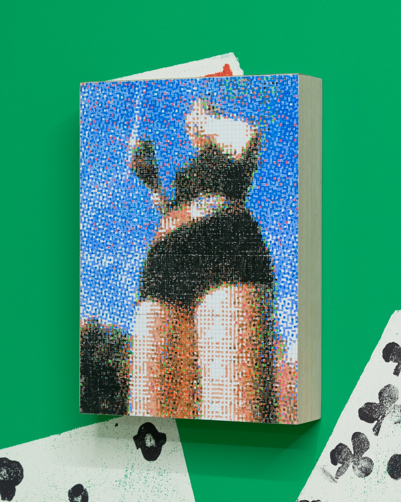 Pixelated painting by Lily Bunney showing a figure in a black crop top against a bright blue background, displayed as a book on a green wall