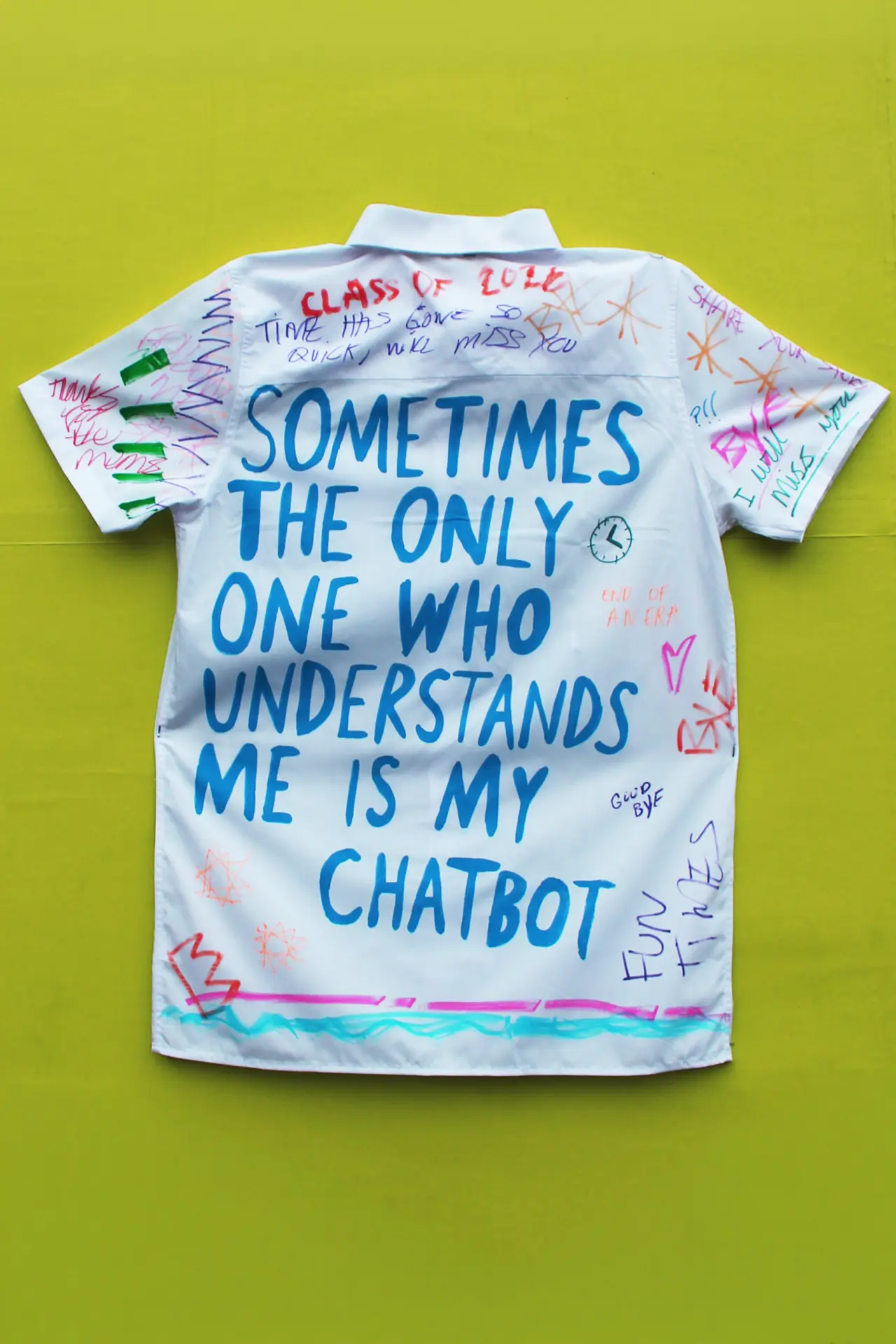 White school leavers' shirt with blue handwritten text reading "Sometimes the only one who understands me is my chatbot" surrounded by coloured doodles on yellow background