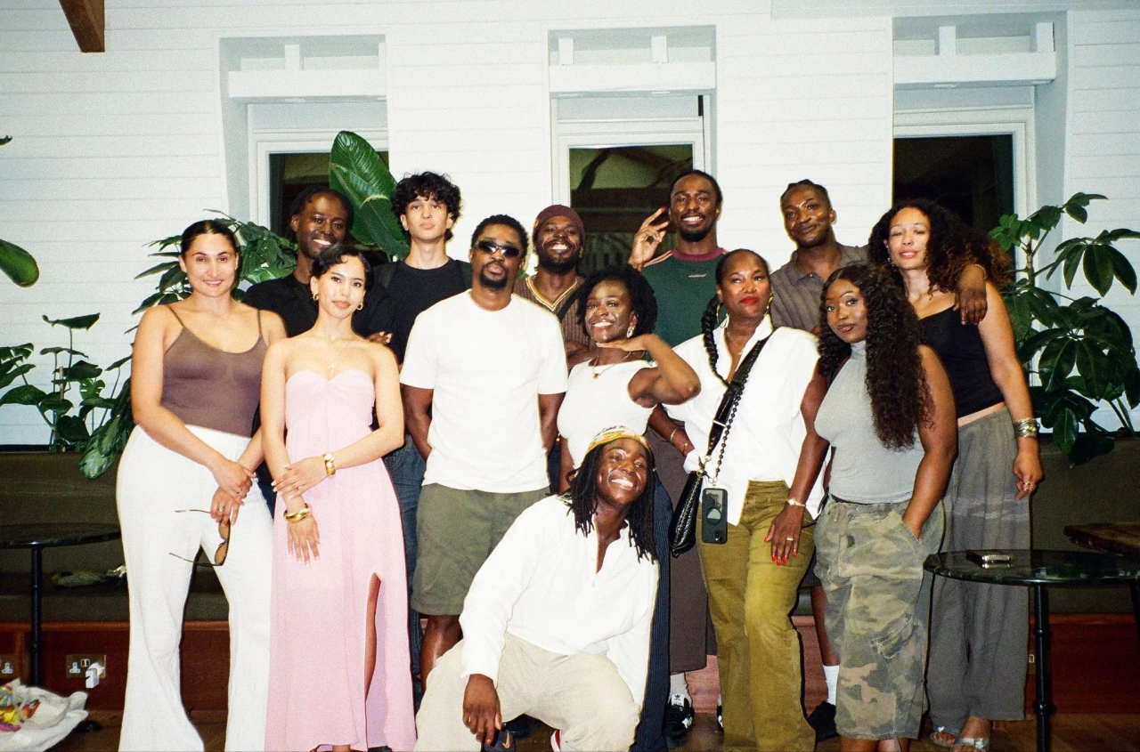 Large group of people posing together indoors in front of white windows and potted plants