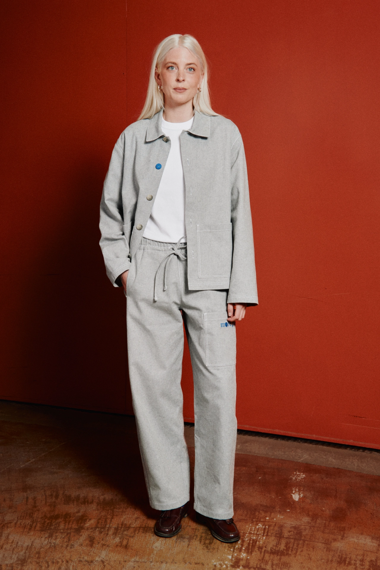 Person wearing light grey Everyday Uniform jacket and trousers with white shirt against a red background