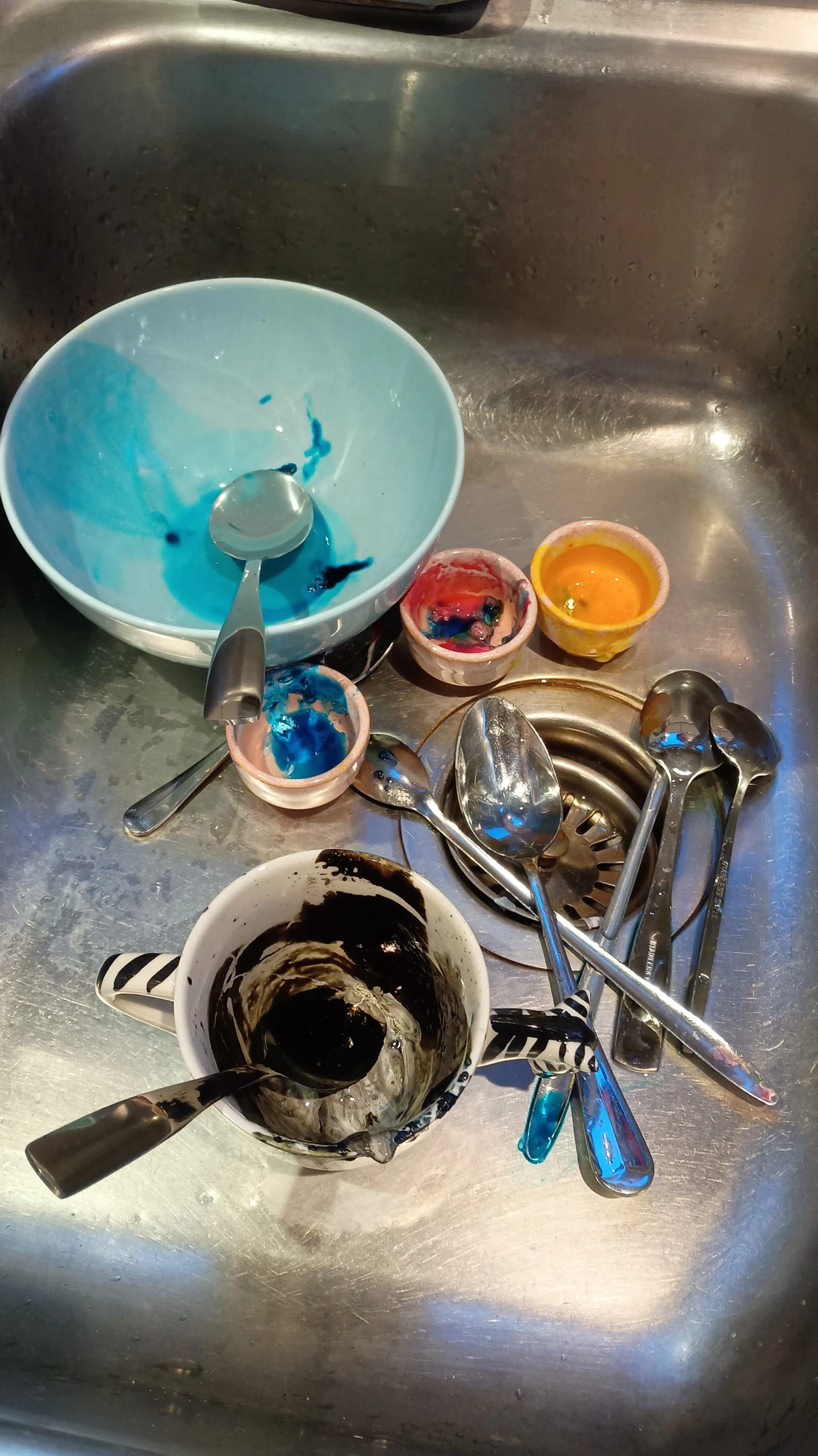 Petri dishes containing coloured mould and fungus arranged in a stainless steel sink alongside spoons and other utensils used in the cultivation process
