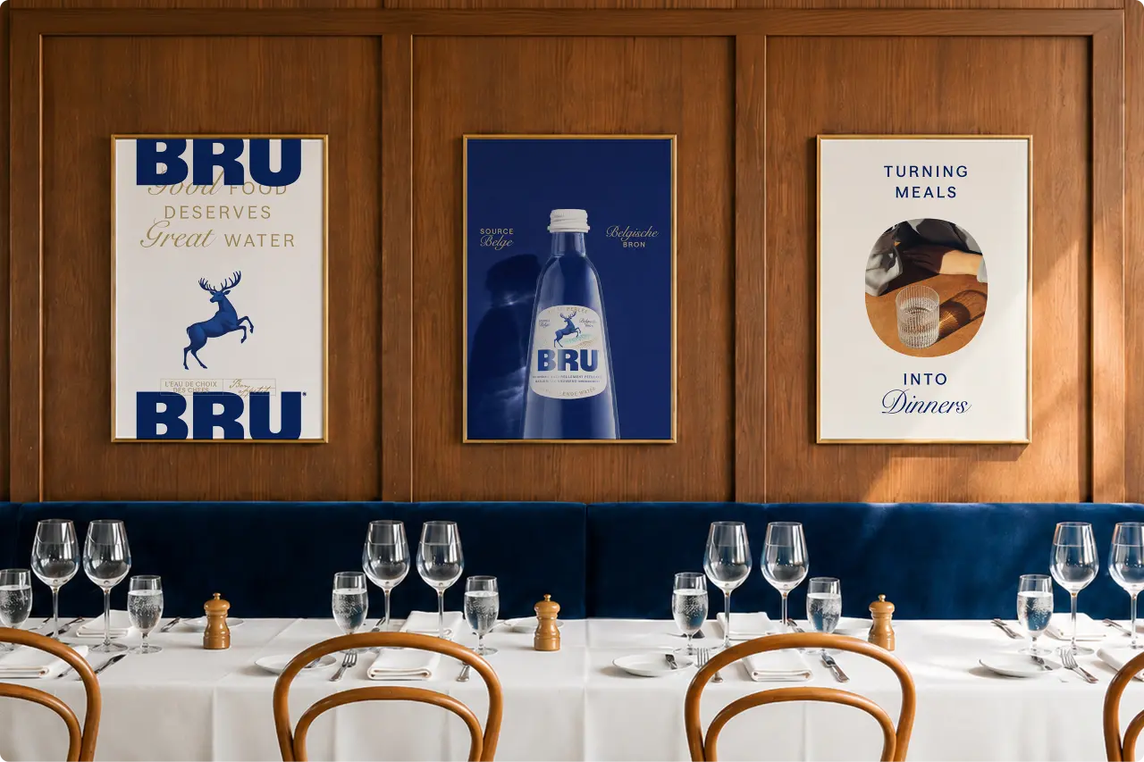Three framed vintage-style BRU sparkling water posters and advertisements displayed on a wood-panelled wall above a formally set dining table with white tablecloths and glassware